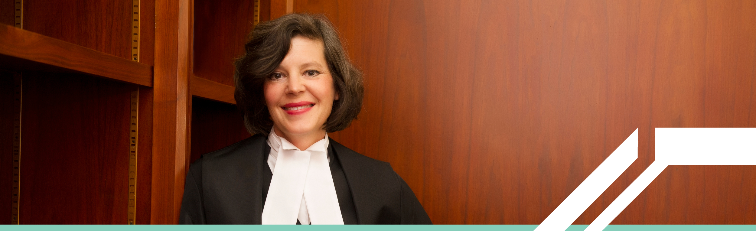 A white woman with wavy brown hair, smiling, wearing judge’s robes