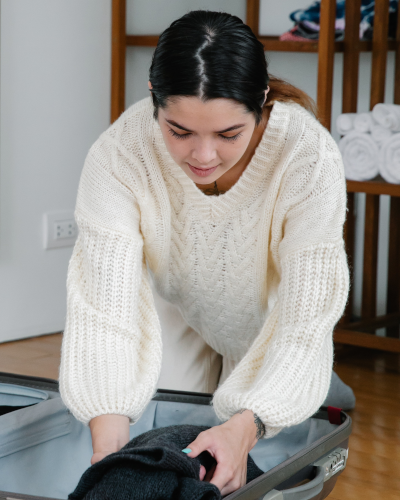 A woman with long dark hair and a white sweater packing a suitcase