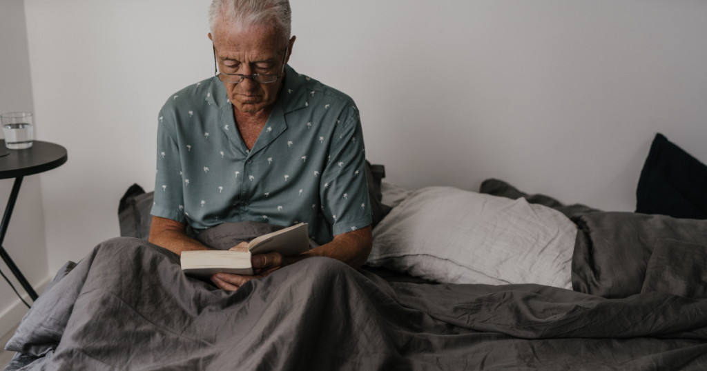 Un homme âgé au lit portant des lunettes et lisant