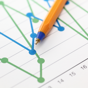 A close up photograph of a pen rested on a paper that has a blue and green line graph