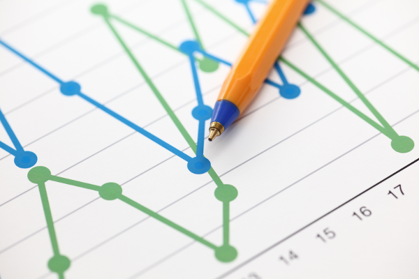 A close up photograph of a pen rested on a paper that has a blue and green line graph