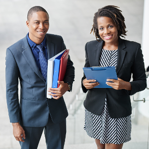 A young Black man in a business suit and an older Black woman in business attire smiling, looking at camera