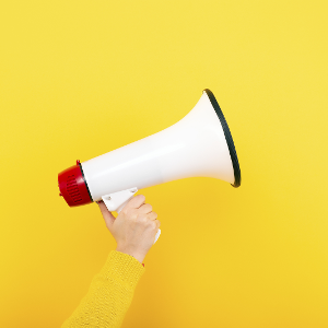 Hand holding a white megaphone in front of a bright yellow wall