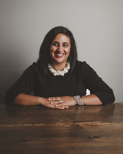 Neha Chugh, wearing a black dress and pearl necklace