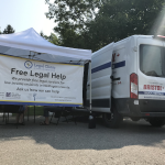 A white ban parked beside a white tent and banner that says Free Legal Help