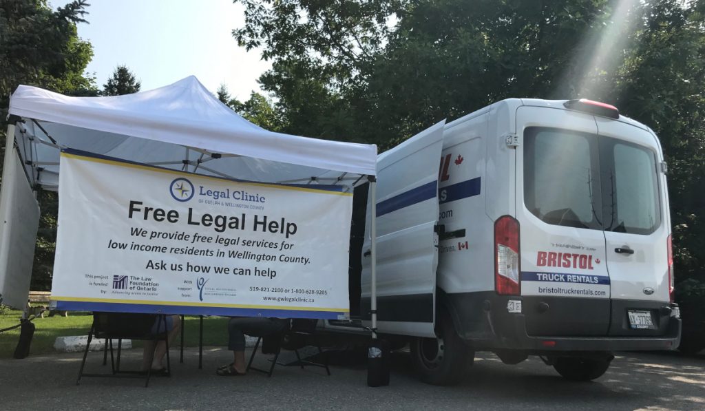 A white ban parked beside a white tent and banner that says Free Legal Help
