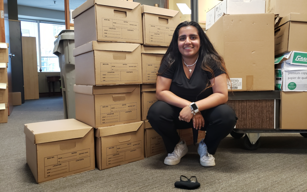 Young woman with long dark hair sitting in front of many moving boxes in a business office