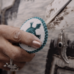Close up of an older woman's hand holding a small artpiece of a beaded turtle and a sacred feather