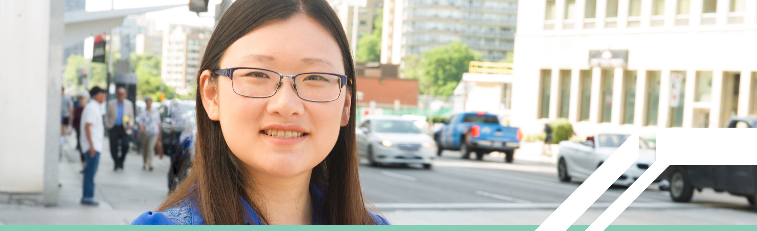 A smiling Asian woman with long, straight black hair wearing glasses and standing near a busy city street