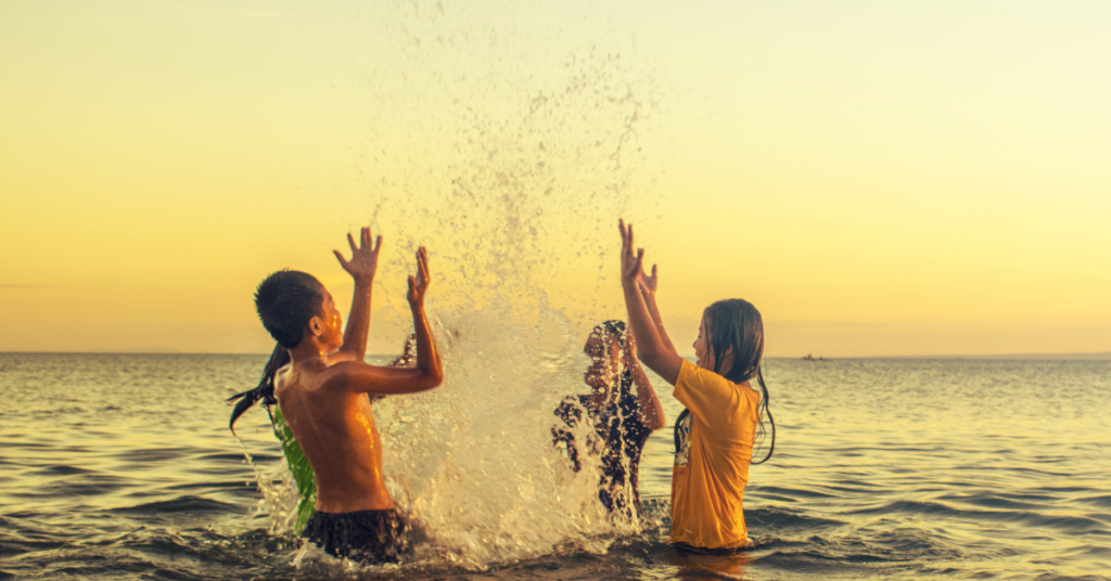 Three children laughing and playing in a large lake at sunset