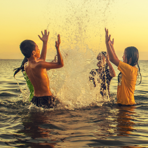 Three children laughing and playing in a large lake at sunset