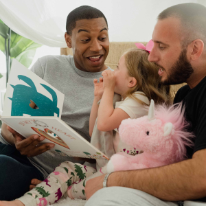 Two men smiling and reading to their young daughter