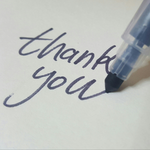 A close up of a blue marker writing 'thank you' on a white piece of paper