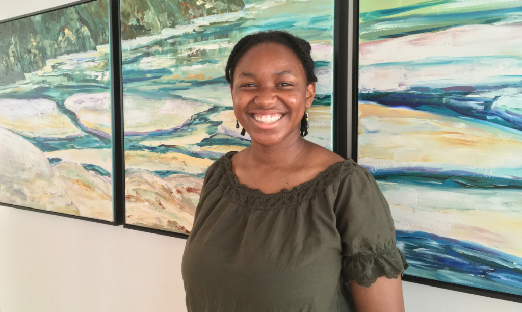 Young woman in green shirt standing and smiling at camera, standing in front of large piece of abstract art