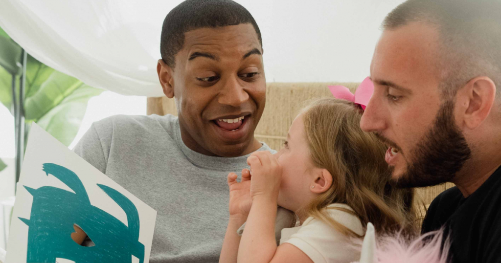 Two men smiling and reading to their young daughter