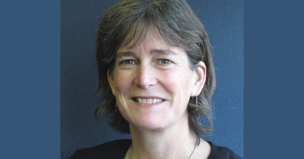 Woman with short grey and brown hair, wearing silver earrings and smiling