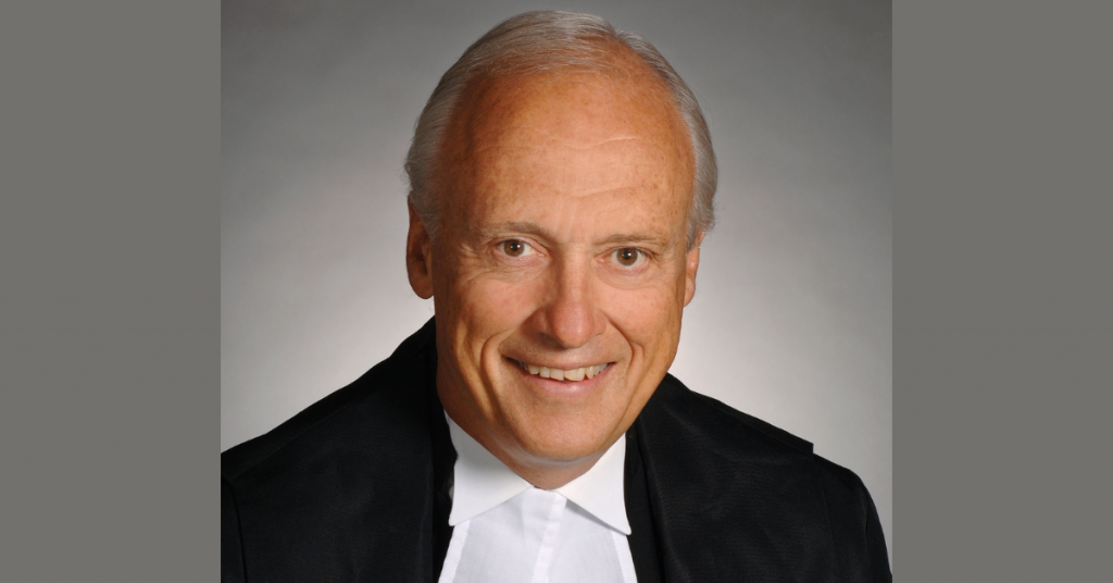 A man with grey hair, smiling and wearing judges robes