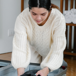 A woman with long dark hair and a white sweater packing a suitcase