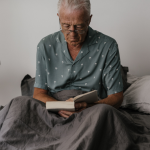 An older man in bed wearing glasses and reading