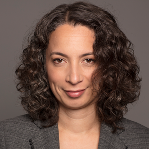 A woman with shoulder length dark curly hair smiling slightly