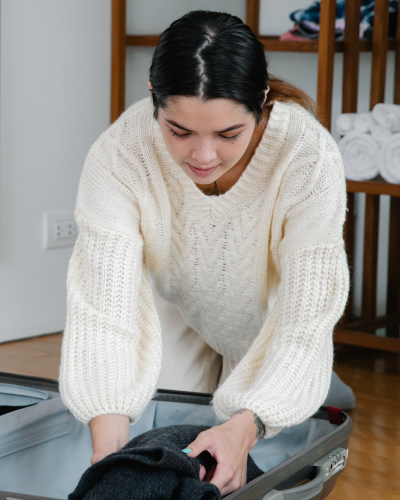 Une femme avec de longs cheveux noirs et un pull blanc faisant sa valise