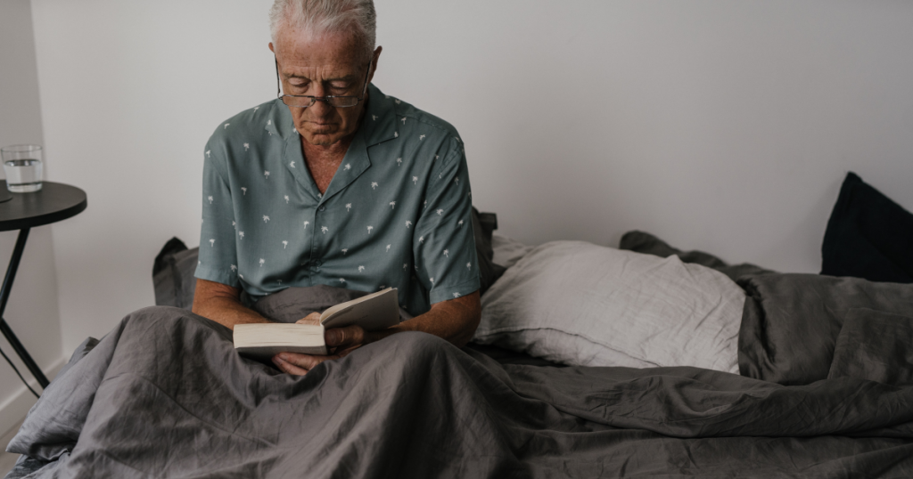 An older man in bed wearing glasses and reading