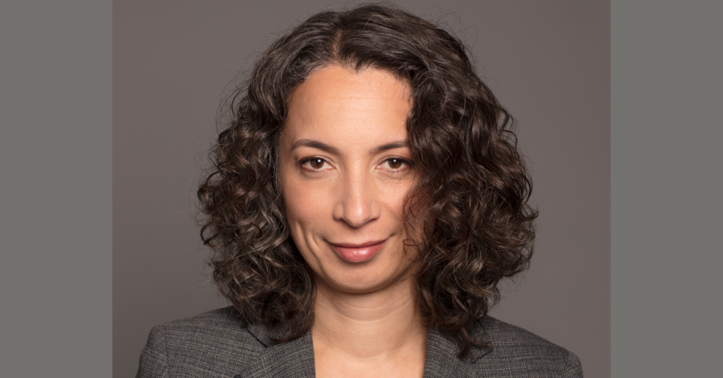 A woman with shoulder length dark curly hair smiling slightly