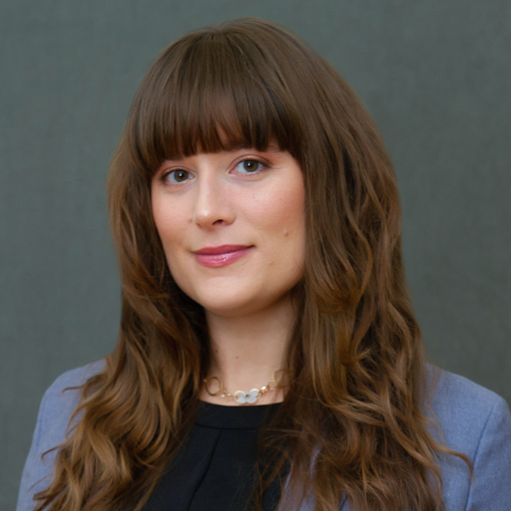 Woman with long, dark brown hair wearing a light blue blazer and black shirt