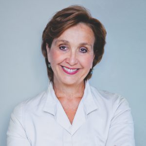 Woman with short brown hair, smiling and wearing a white shirt