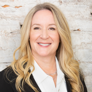 A woman with long blonde hair, smiling and wearing a white shirt and black blazer