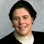 Woman with short black hair wearing a cream coloured blouse and black jacket