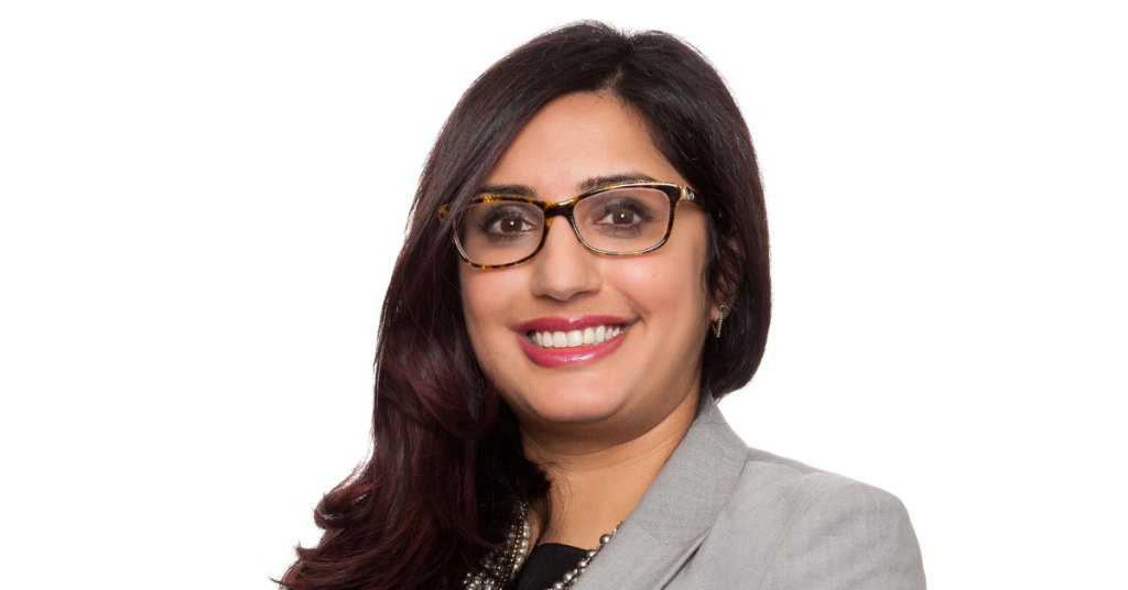 Woman with long thick brown hair, wearing glasses, smiling into camera