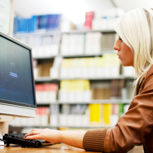 Woman with very light blond hair working on a computer with shelves of books in the background