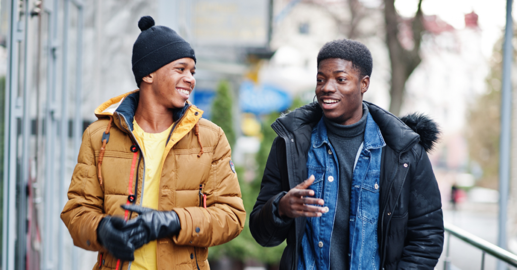 Two young Black men dressed in winter clothes, walking and laughing together