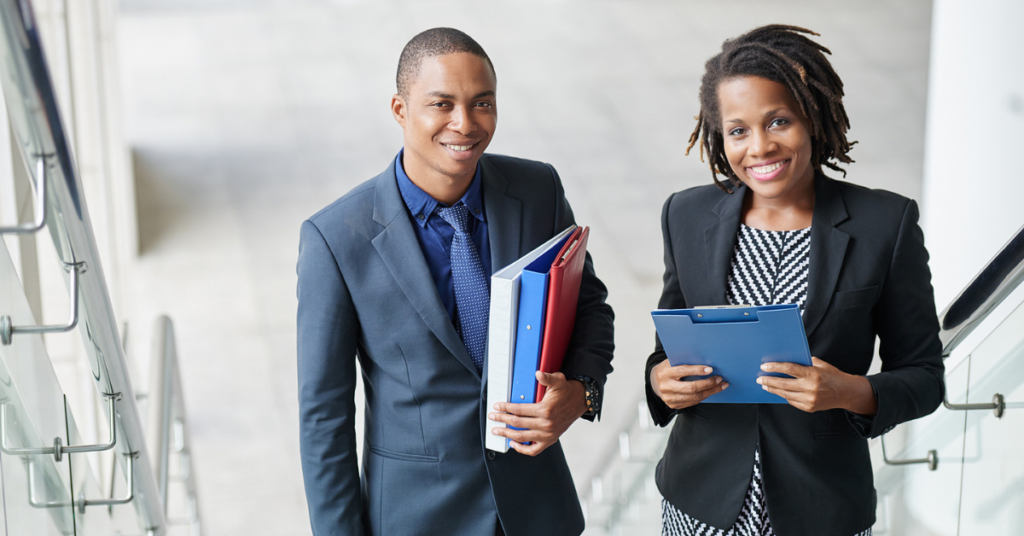 A young Black man in a business suit and a Black woman in business attire smiling, looking at camera