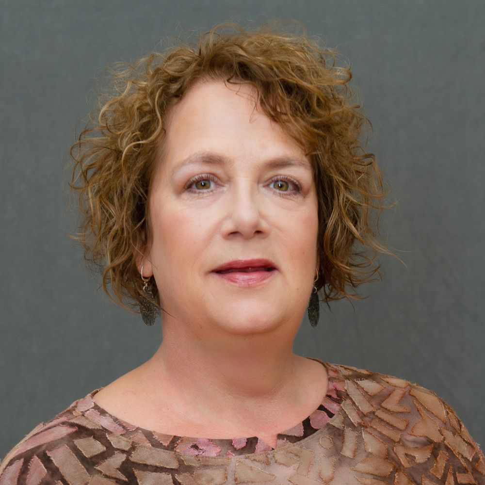 Women with short, light brown curly hair wearing a brown top