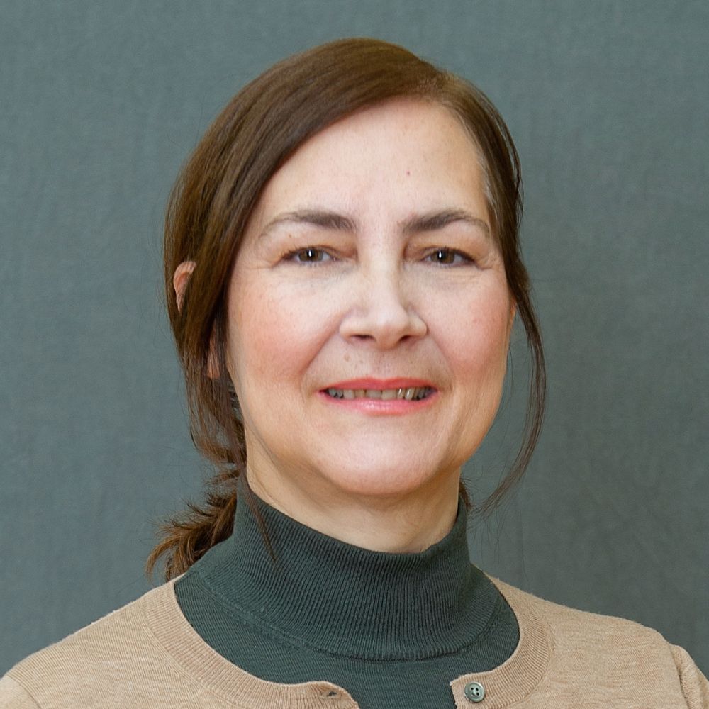 Woman with chestnut brown hair tied back in a low ponytail wearing a green and beige top