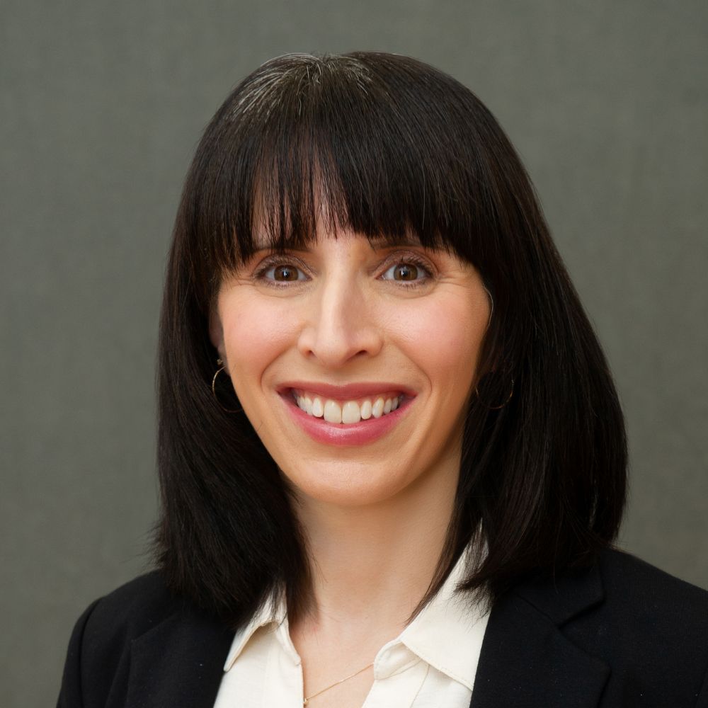 Woman with shoulder-length black hair wearing a black jacket and white shirt