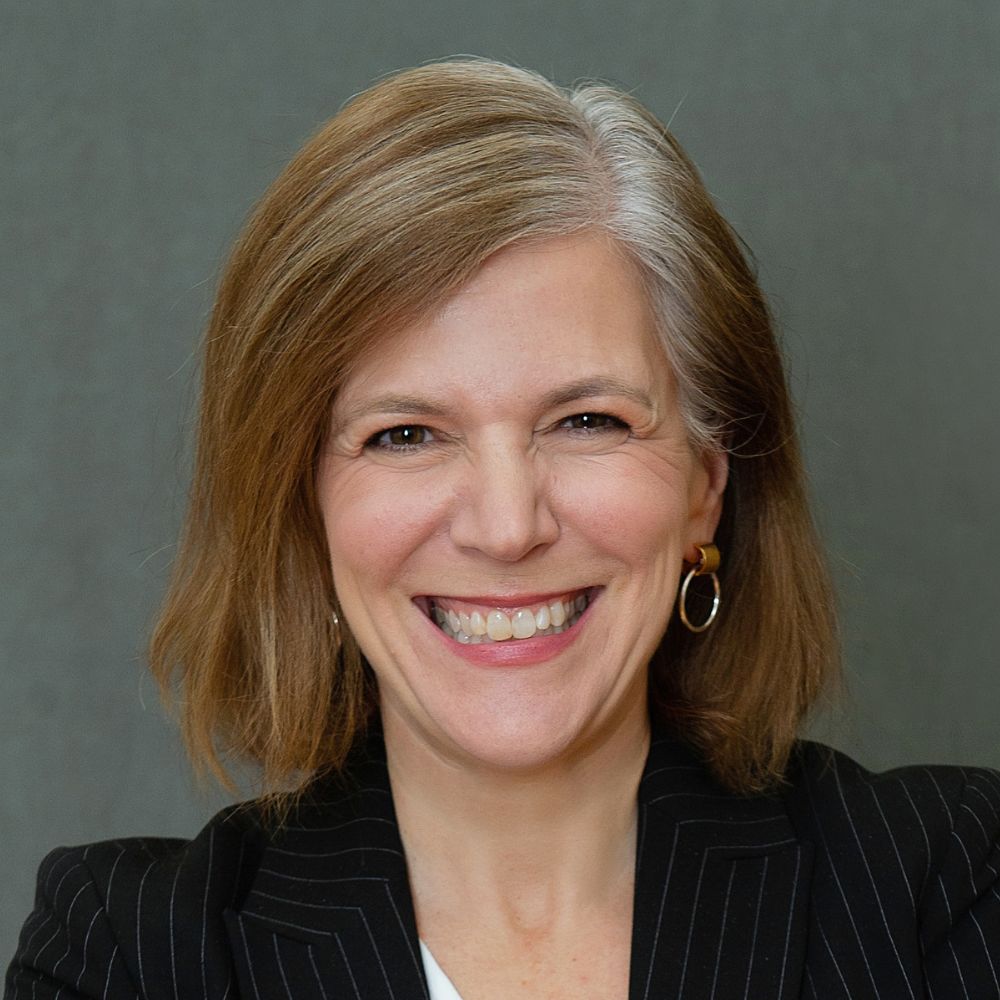 Woman with light brown and grey hair wearing a black jacket and white shirt