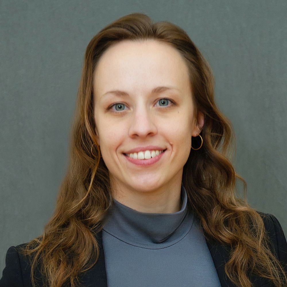 Woman with long, wavy brown hair wearing a black jacket and grey shirt