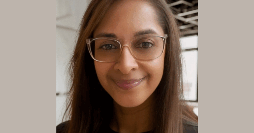 A woman with long brown hair who is smiling and wearing light-coloured glasses