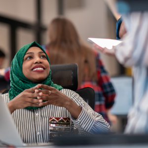 Woman wearing a green hijab talking with a co-worker in an office