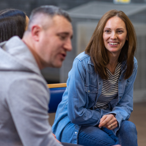 A man and a woman sitting in a circle of chairs inside a large community centre